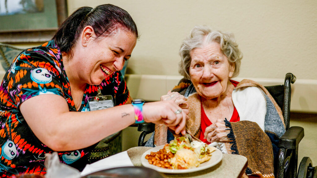 A nurse assisting a woman at a skilled nursing facility during dinner