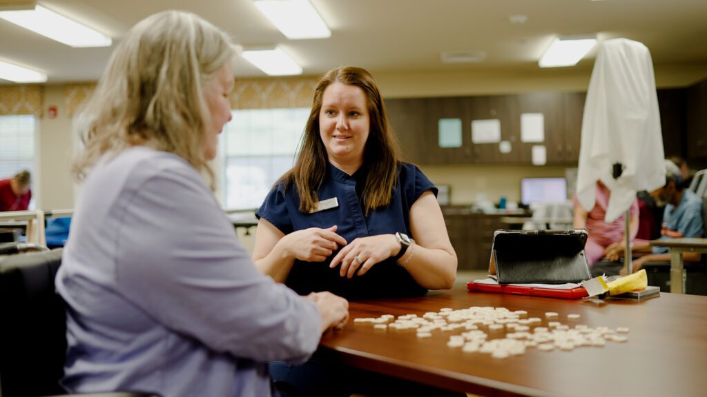 A nurse assists a woman in an activity at a long term care facility