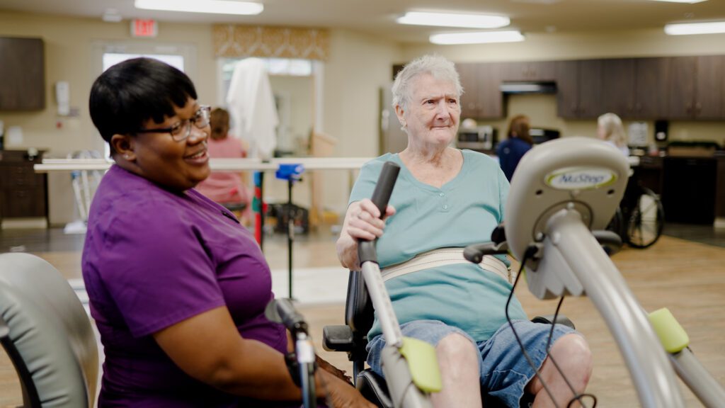 A woman using gym equipment with the assistance of a nurse at a short term care facility